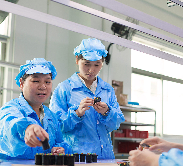 Workers assembling electronic components in cleanroom attire.